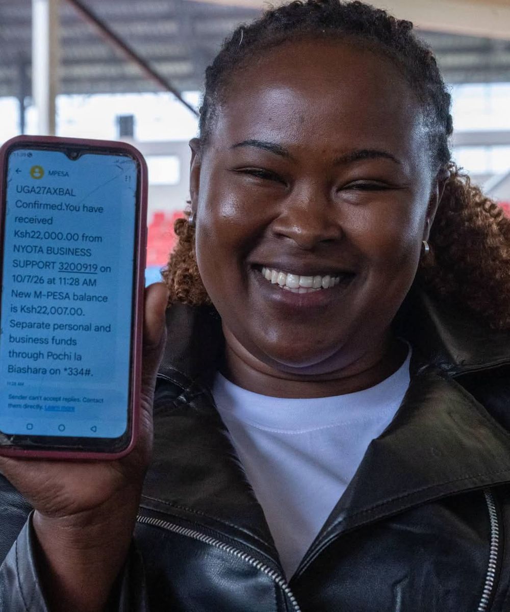 A young NYOTA business support beneficiary smiles and holds up her phone showing the payment confirmation.